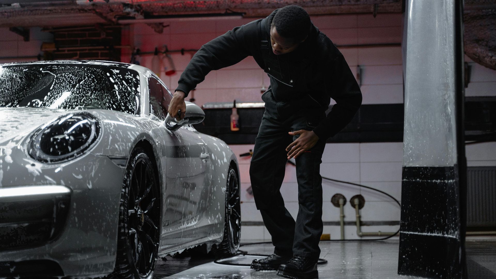 Man washing a luxury car in an indoor garage, emphasizing automotive care.