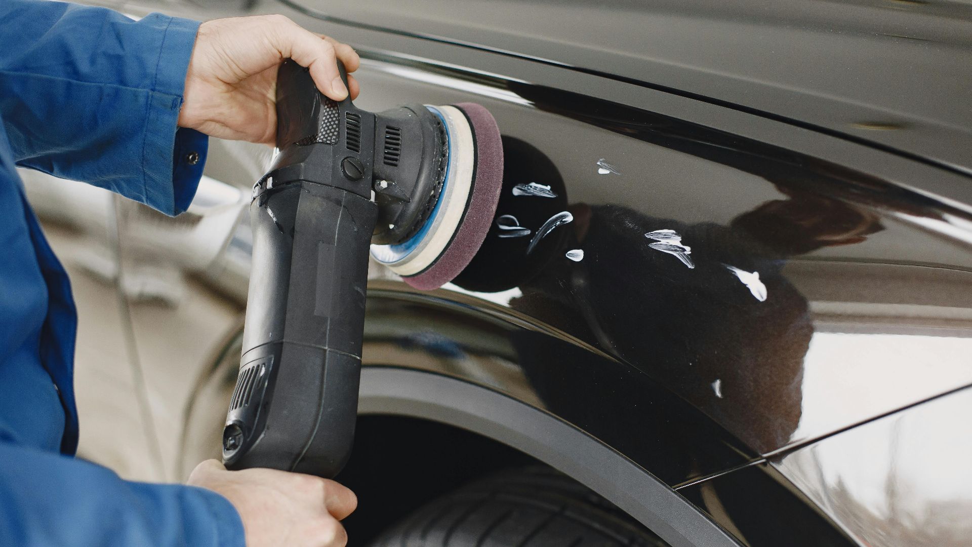 Hands using a polishing machine on a car's surface in a garage setting.