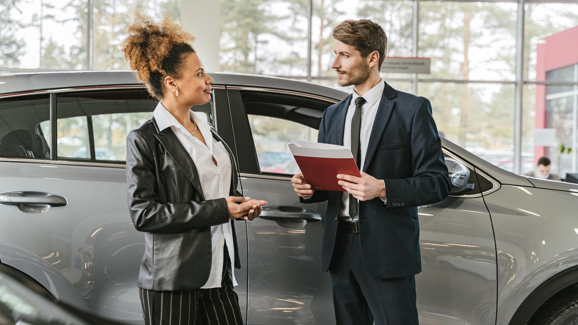 A woman discussing car purchase with a dealer inside a car dealership showroom.