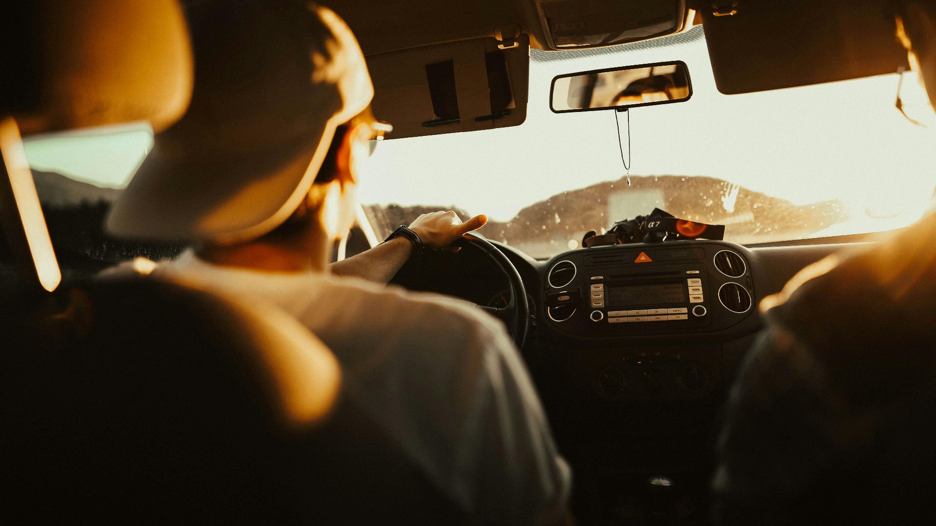 Man driving car with passenger at sunset, capturing warm sunlit atmosphere.