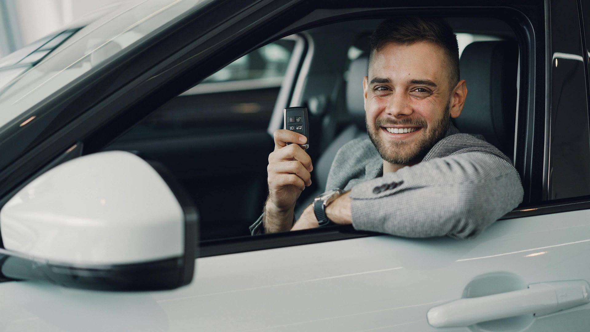 Happy young man holding car keys inside a vehicle. Perfect image for car rental or sales.
