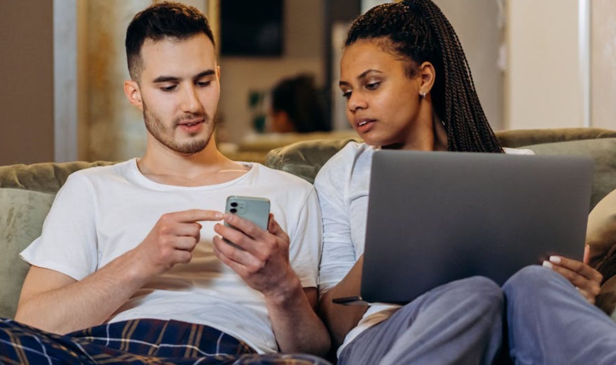 A Woman Holding a Laptop Beside a Man Holding a Cellphone