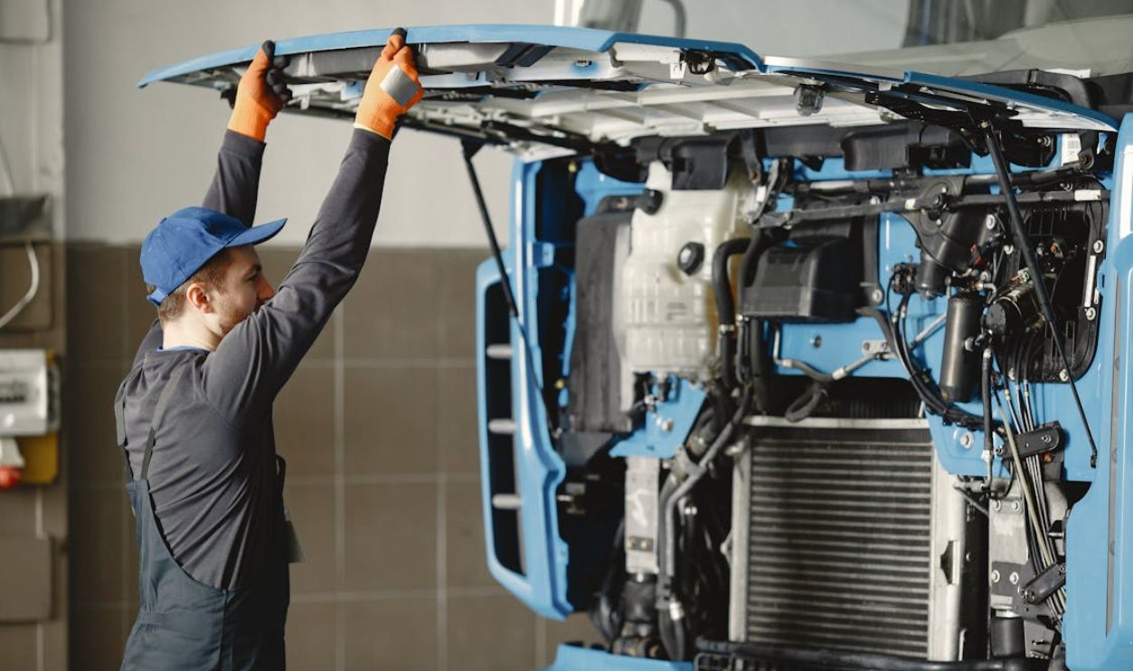 Man in Working Clothes Looking Under the Hood of Blue Truck