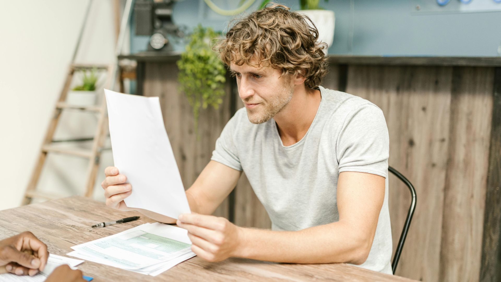 A man with curly hair evaluates documents at a desk, highlighting focused work in a professional setting.