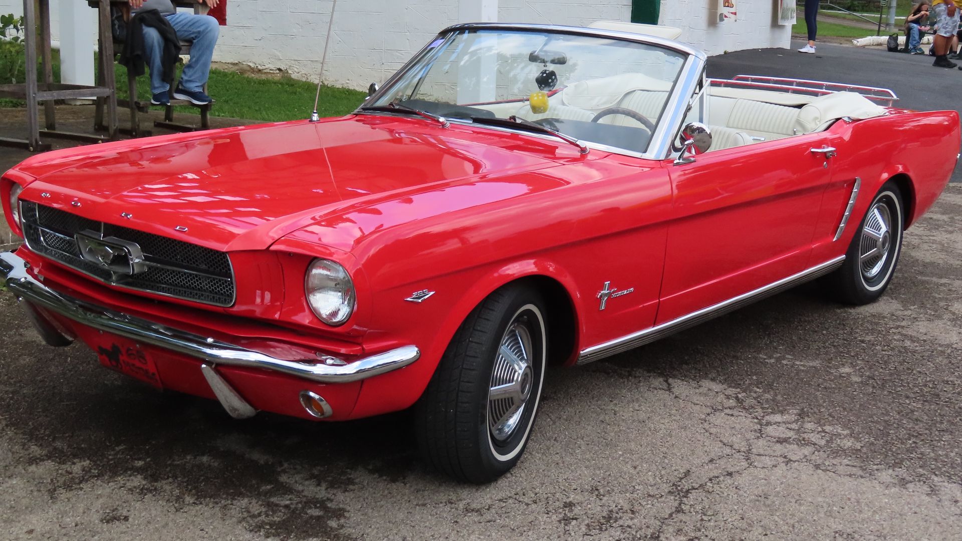 1965 Ford Mustang base convertible photographed at a car show in New Castle, Pennsylvania. This Mustang is finished in Rangoon Red and powered by the 289 ci Ford Windsor V8 engine. Its wheels feature one of multiple hubcap designs that were offered in 1965.