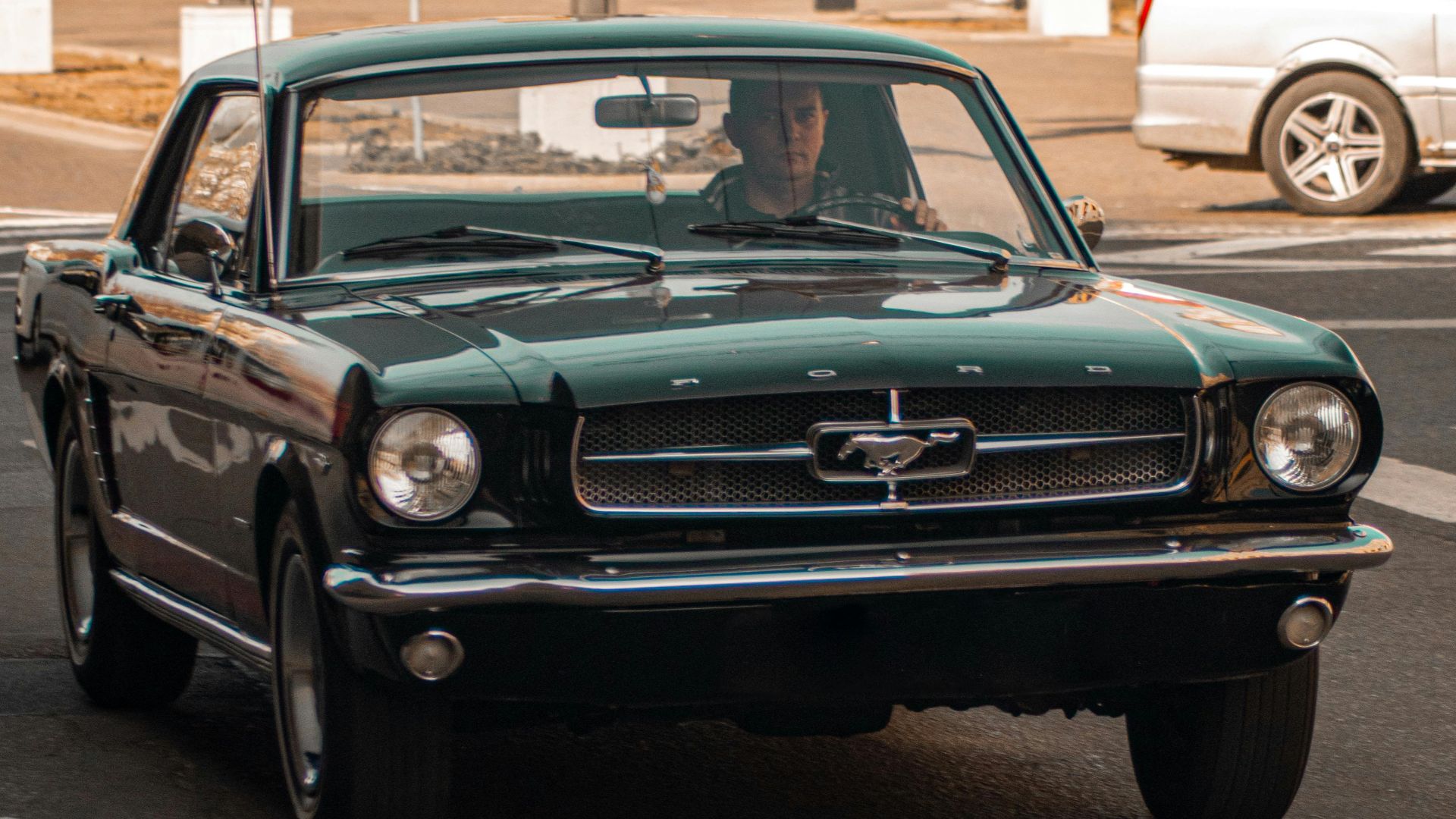 Vintage green Ford Mustang driving through a European town square on a sunny day.
