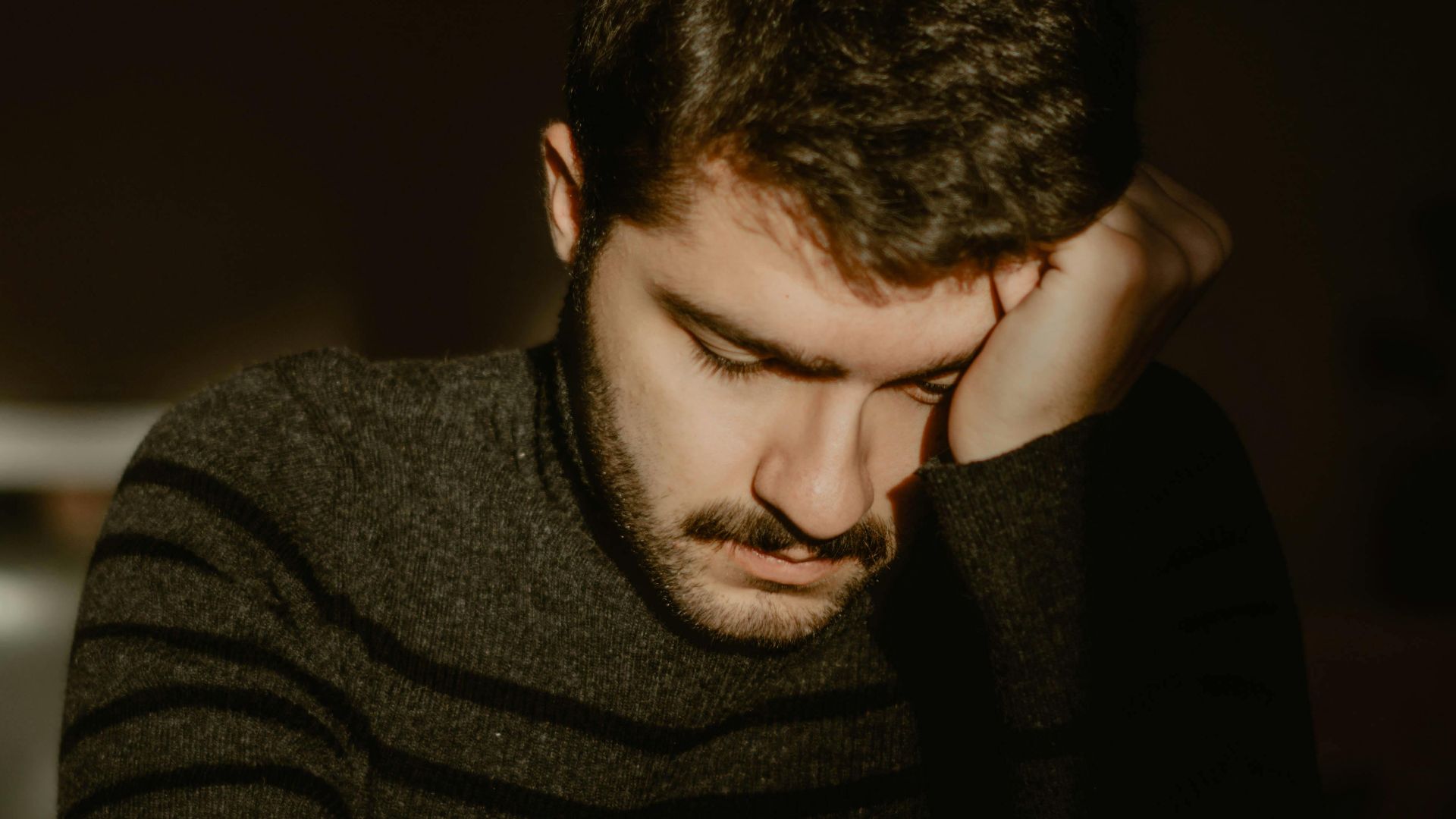 Portrait of a young man sitting alone indoors, reflecting in a dimly lit room.