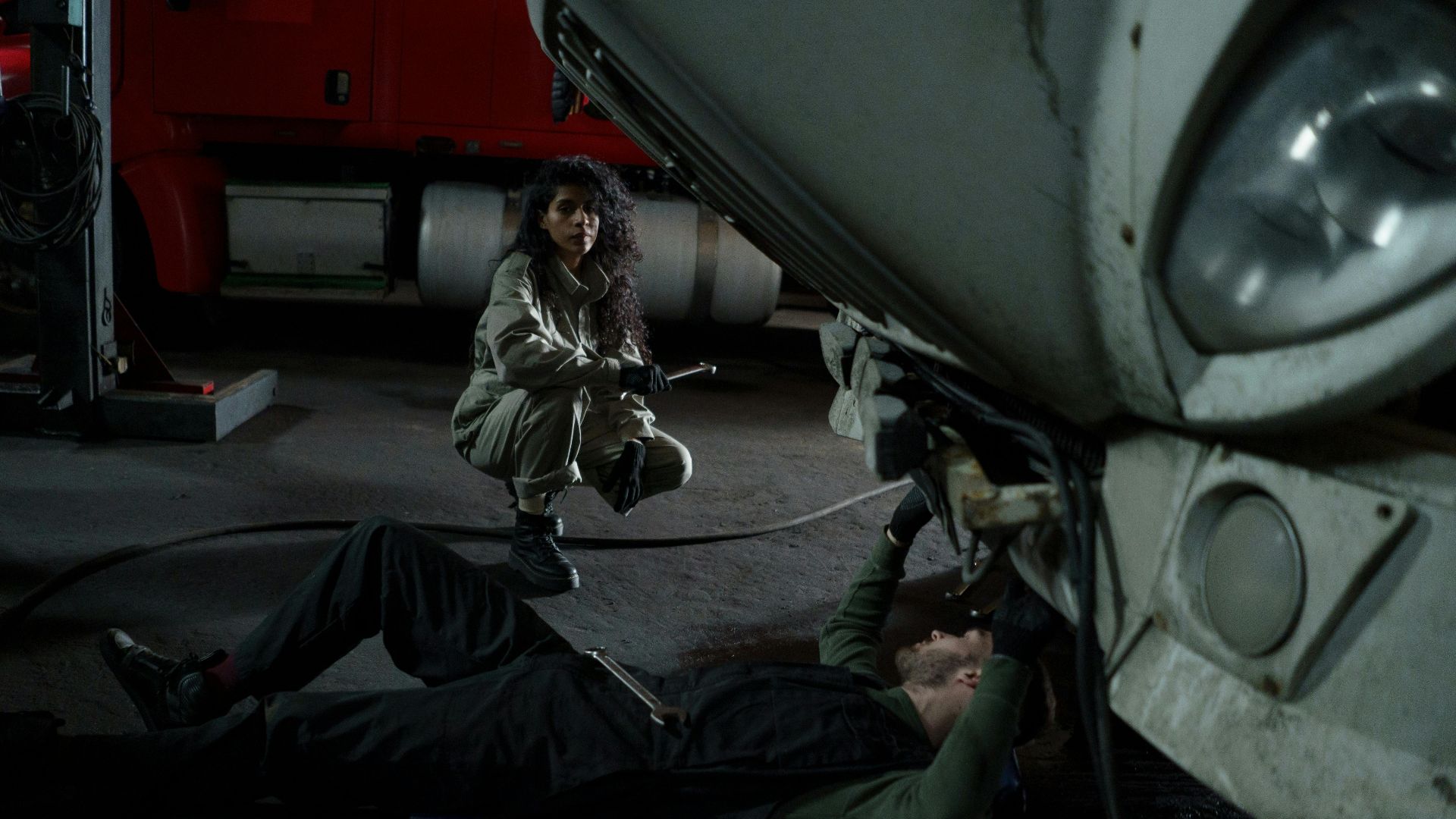 Two mechanics performing maintenance on a truck inside a garage setting.