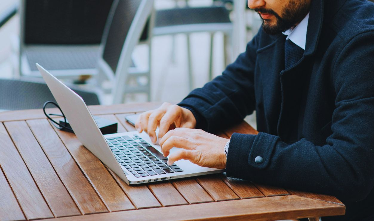 Serious ethnic businessman typing on laptop on cafe terrace