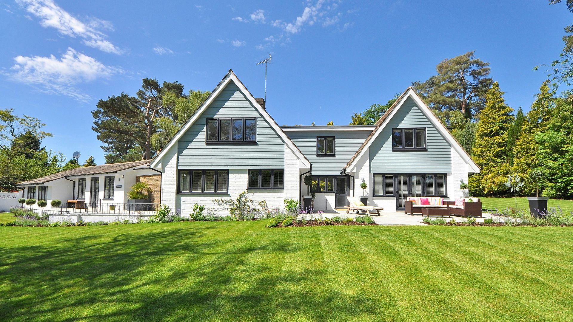 Modern family home exterior showcasing a large lawn and garden under a clear blue sky.