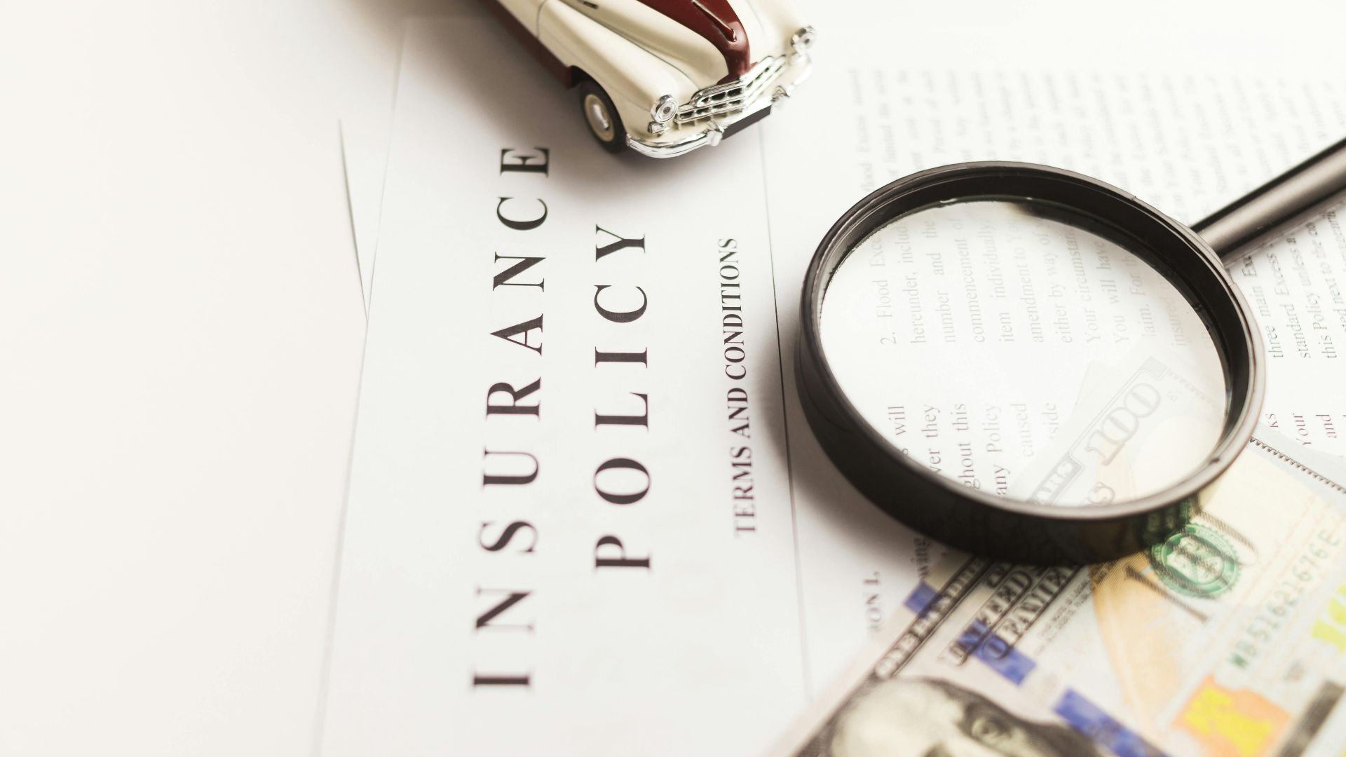 Close-up image of an insurance policy with a magnifying glass, money, and toy car.