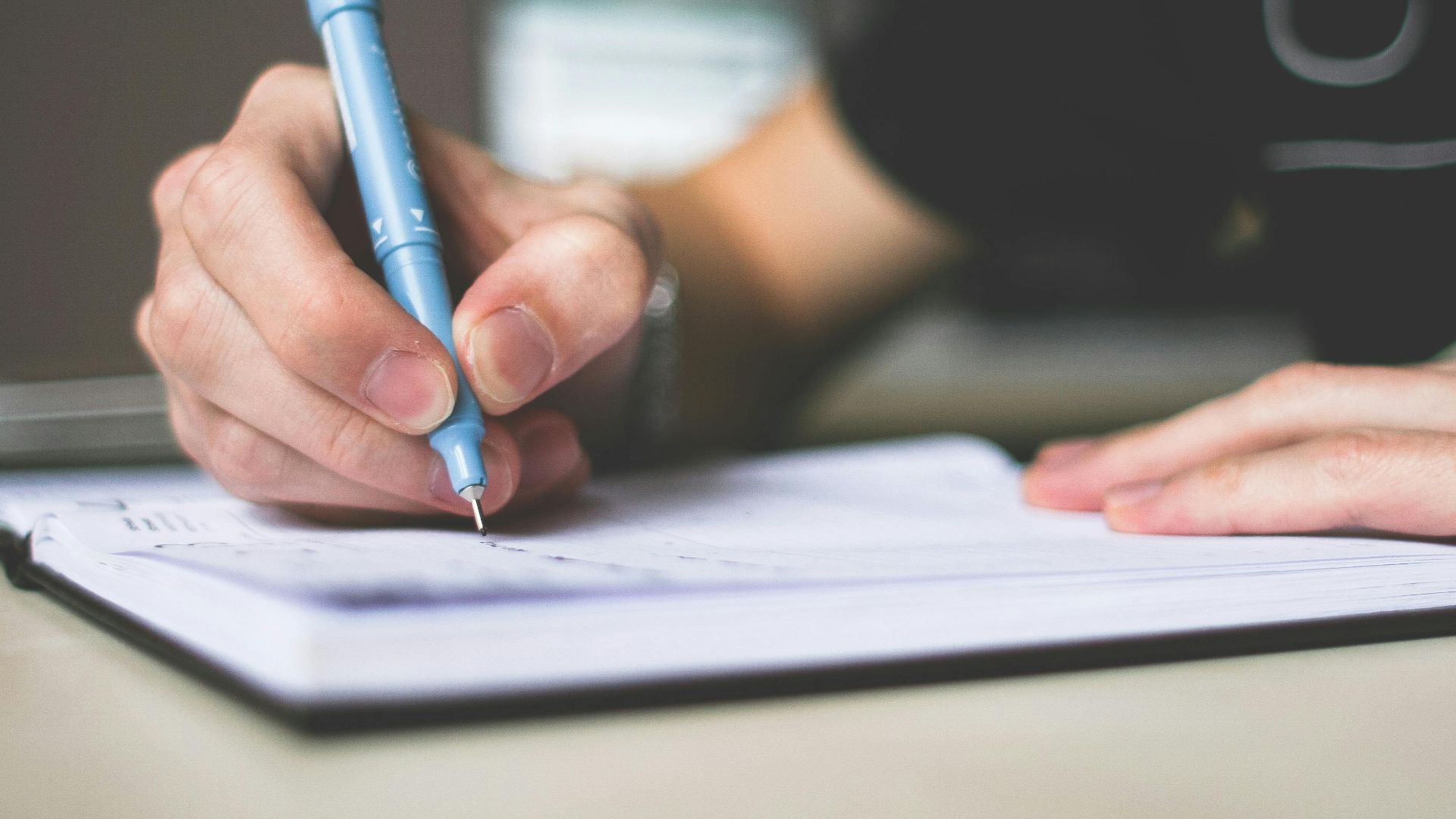 Close-up of hand writing in notebook using a blue pen, focus on creativity.