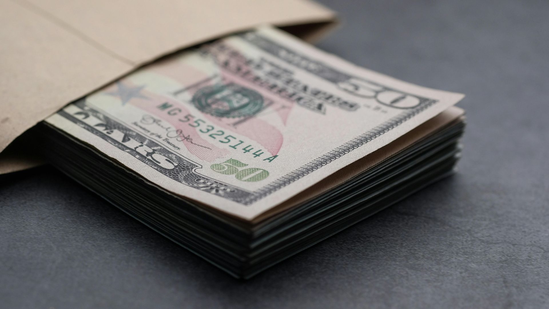 Close-up of US fifty dollar bills partially enclosed in a brown envelope, symbolizing finances.
