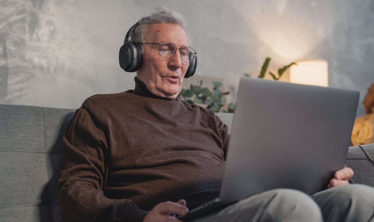 Man in Brown Sweater Wearing Black Sunglasses Using Laptop