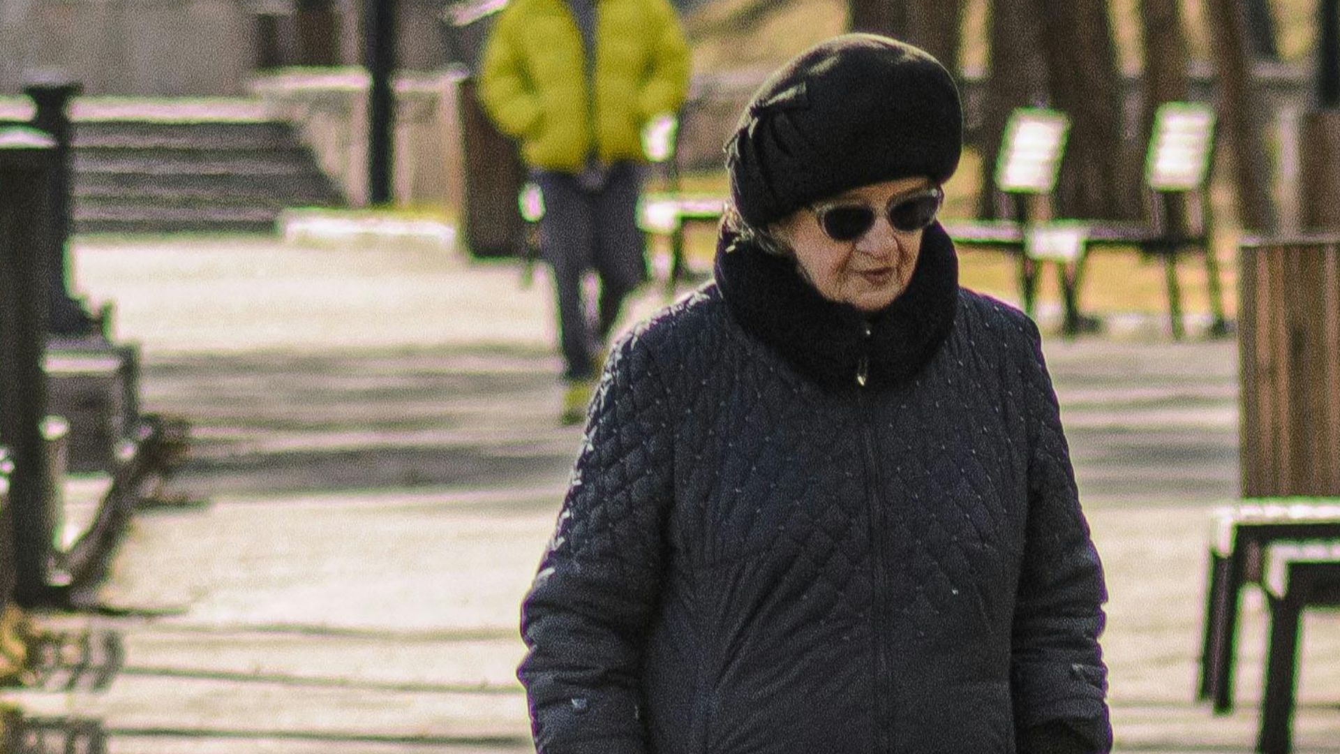 Two senior women stroll in an outdoor park on a sunny early spring day.