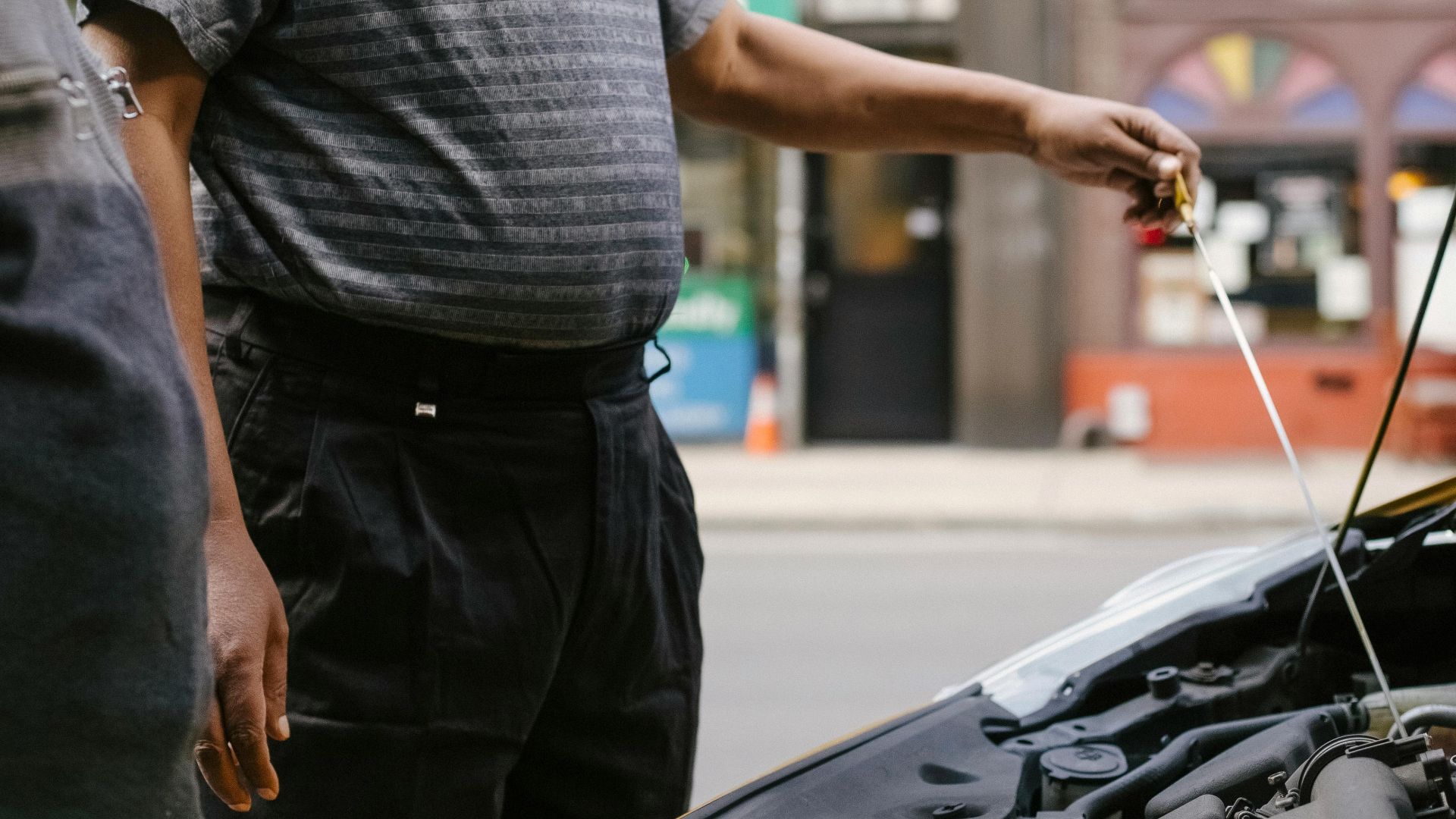 Two men inspecting a car engine on an urban street, focusing on maintenance.
