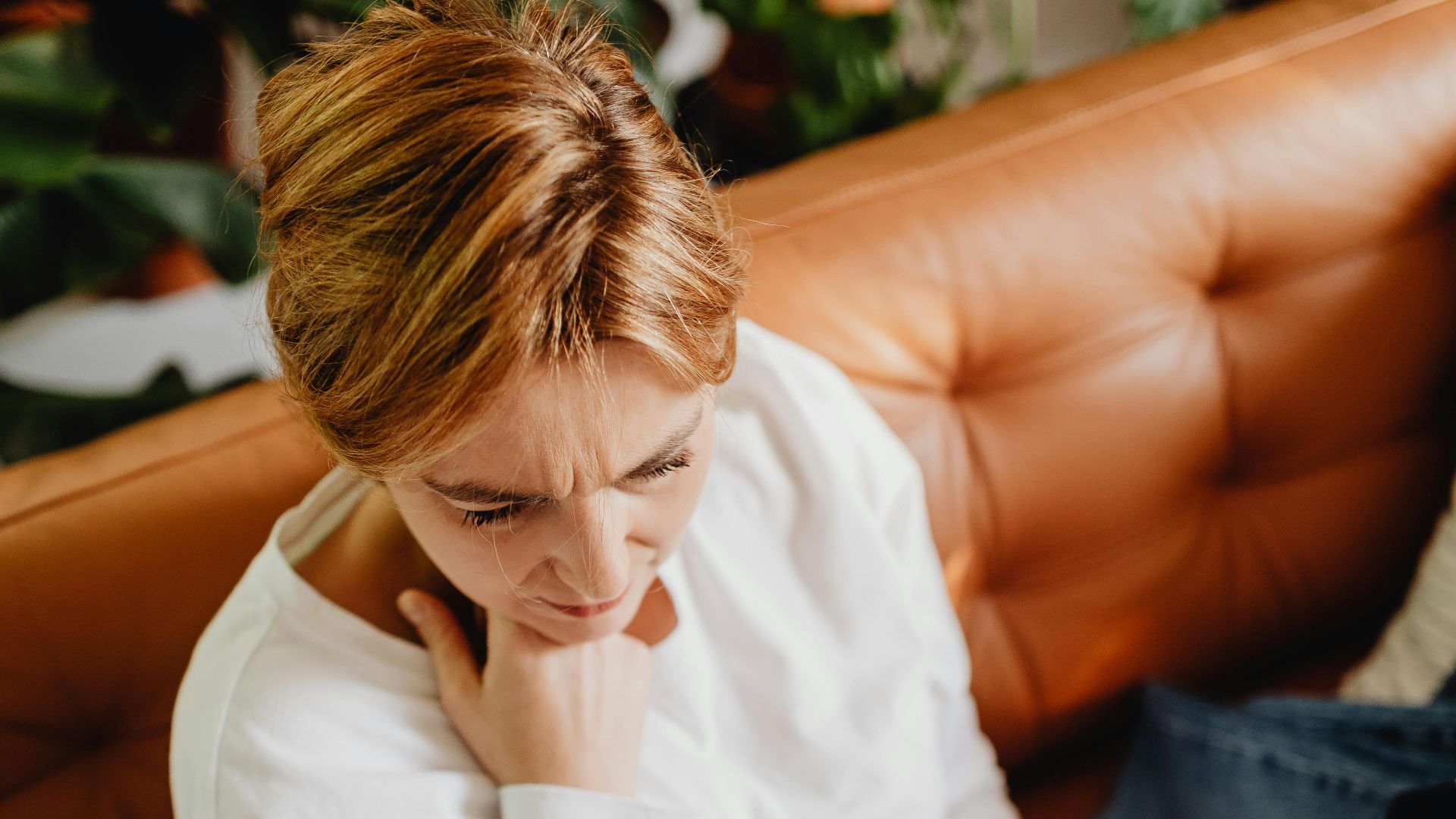 Woman sitting on a sofa looking worried while using her phone, surrounded by clothes indoors.