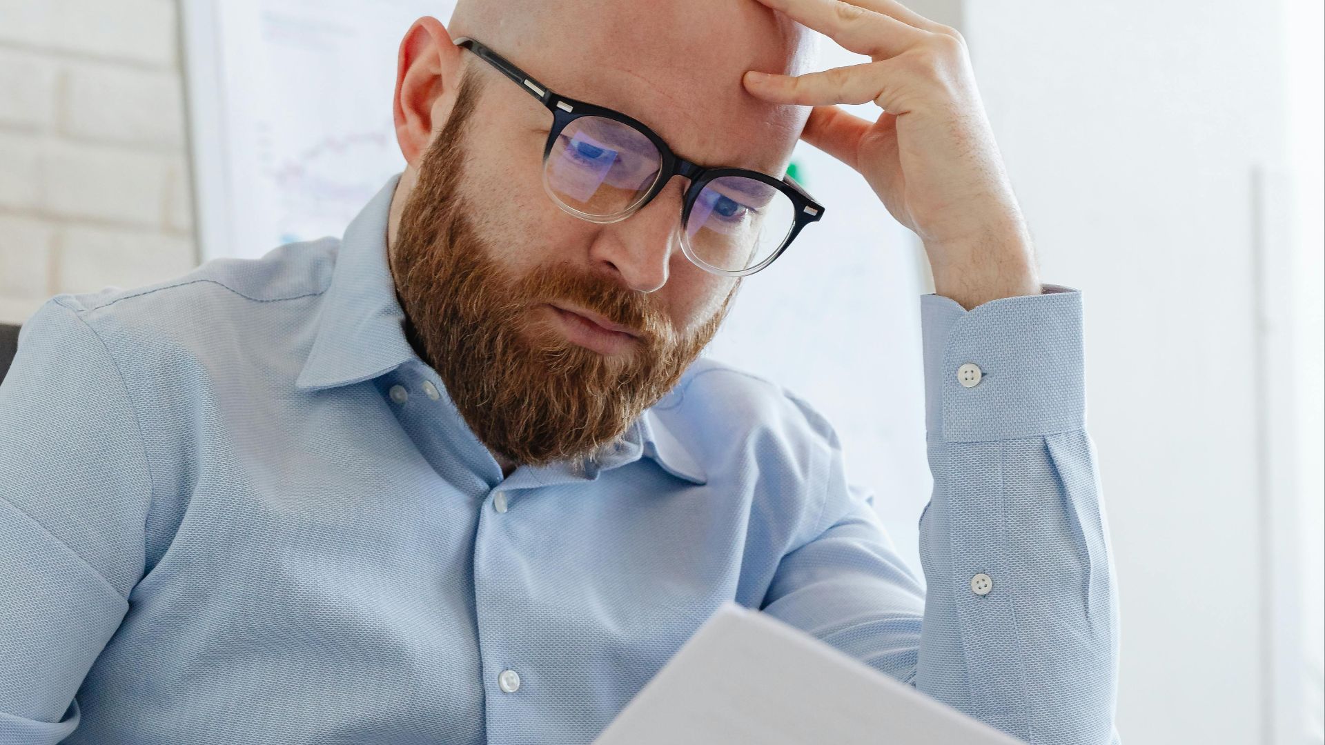Caucasian businessman with beard and glasses reviewing documents in a modern office setting.
