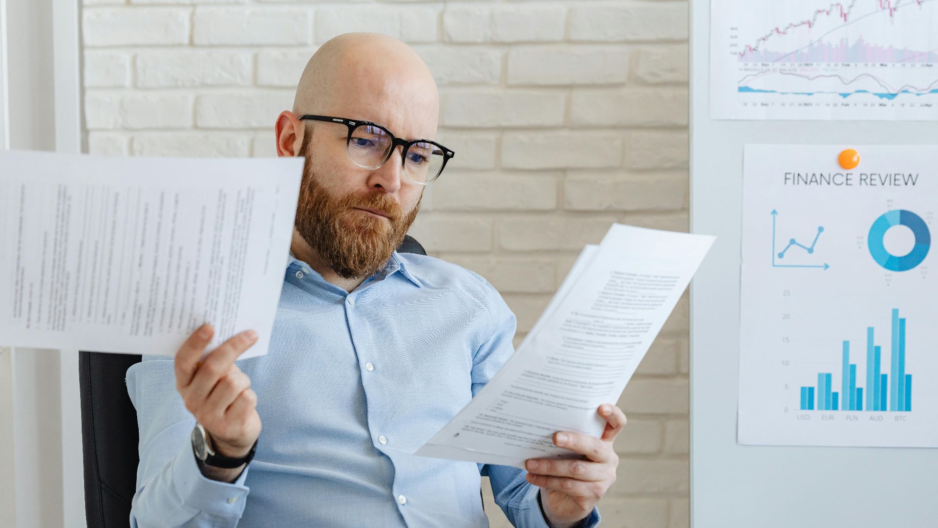 Bald bearded businessman reading financial documents in modern office setting.