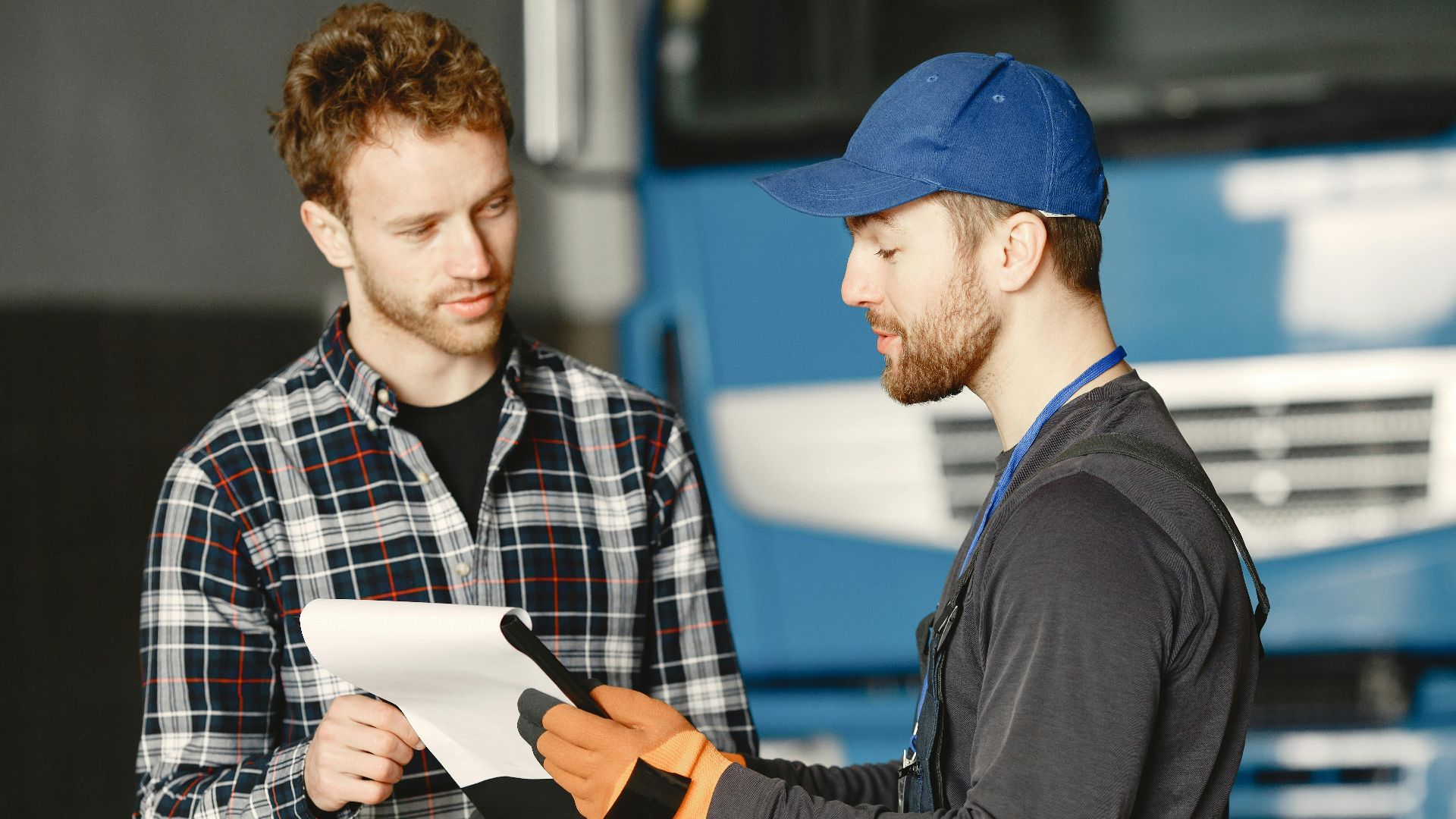 Mechanic in uniform talks with a customer about vehicle maintenance inside a garage.