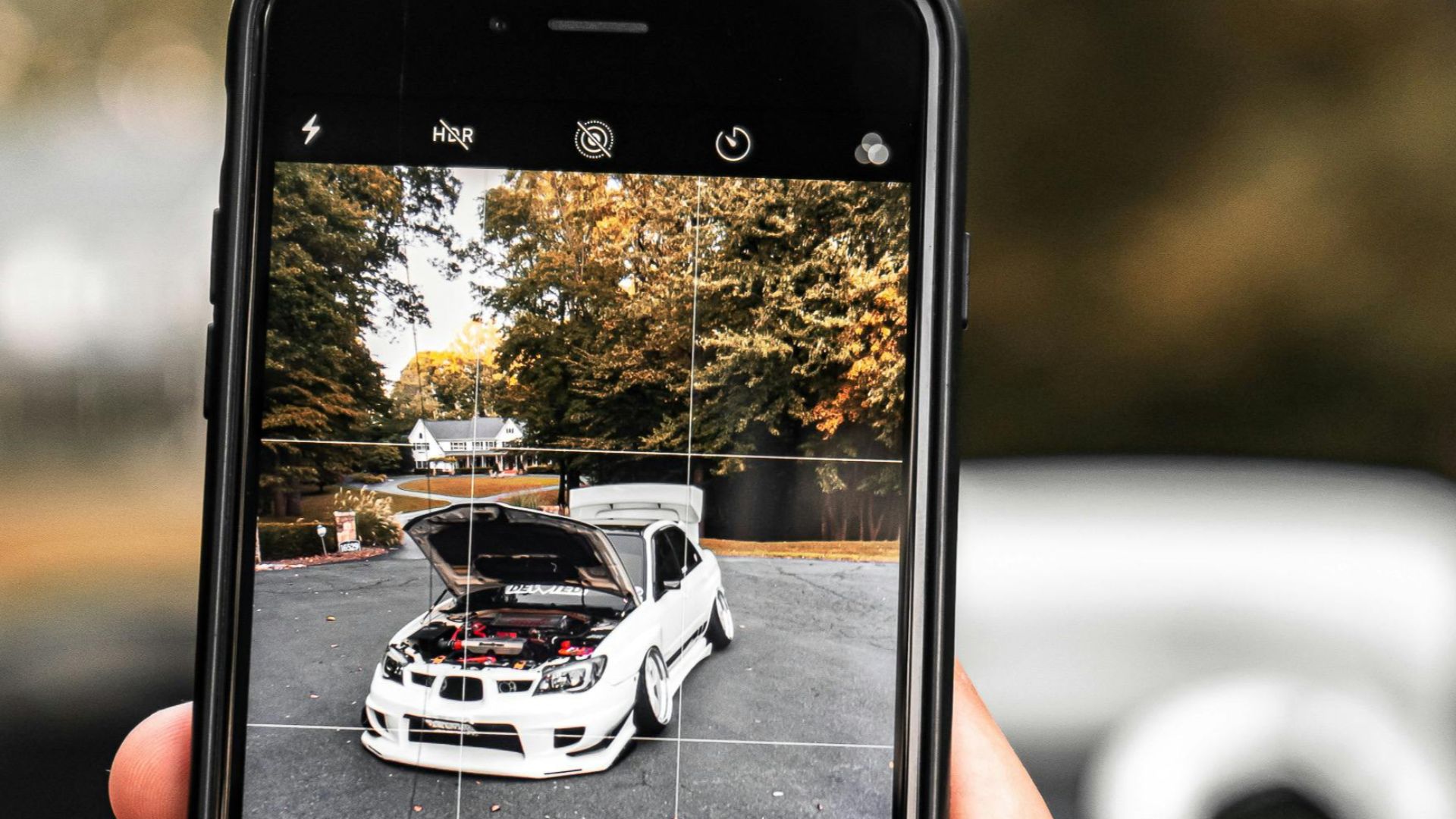 Person photographing a white car outdoors with a smartphone, showing technology and leisure.