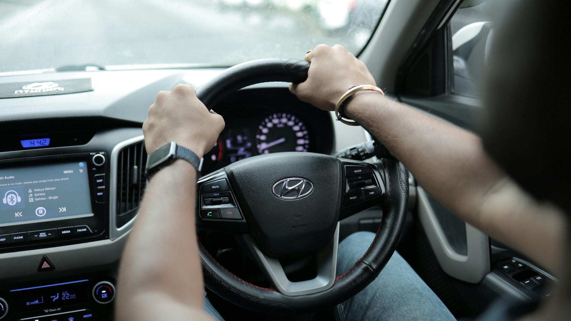 Close-up of a person's hands on a car steering wheel, highlighting the dashboard and interior features.
