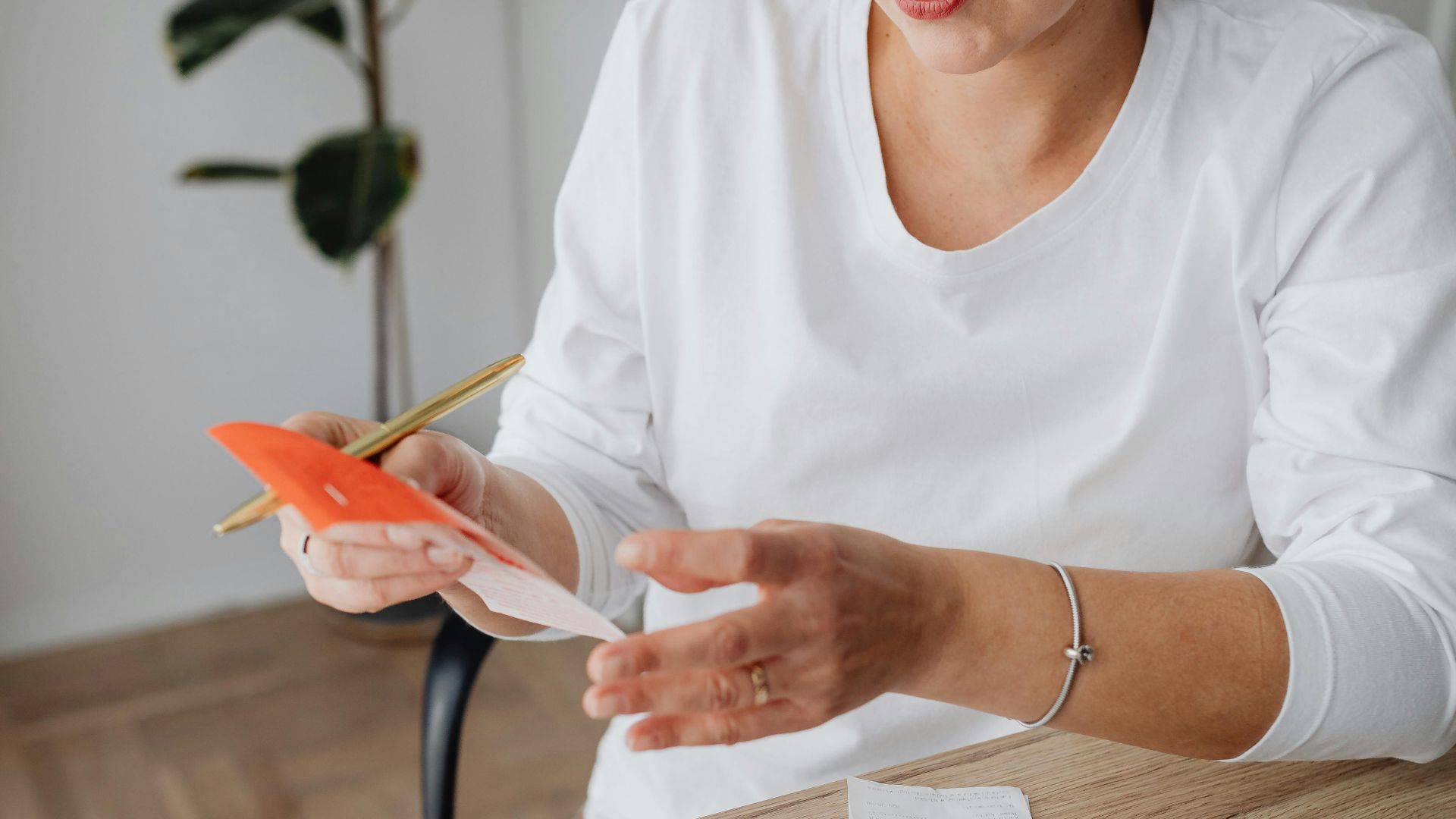 Woman calculating expenses with calculator and notebook at home office, surrounded by receipts and money.