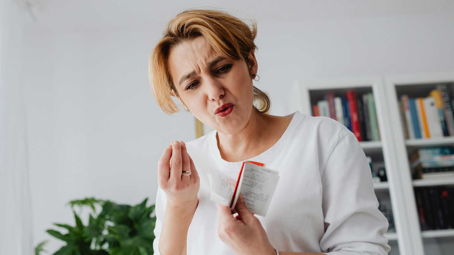 A concerned woman reviews her finances while holding receipts, showing a worried expression.