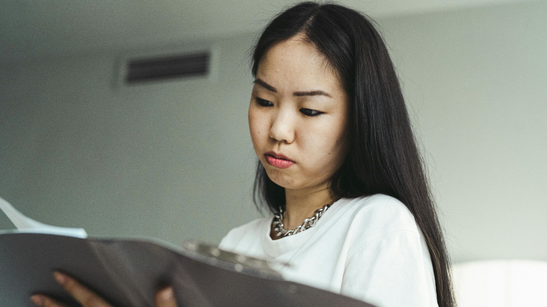 Asian woman in casual attire examining paperwork with concentration indoors.