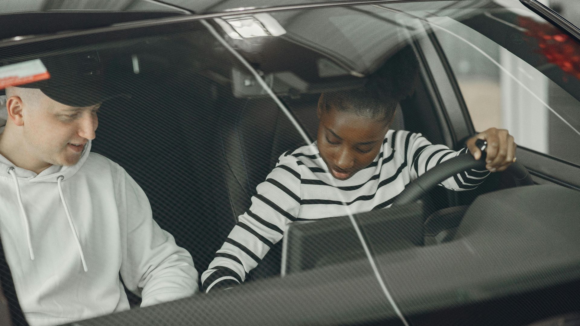 Black woman and caucasian man sitting inside a vehicle, discussing driving.