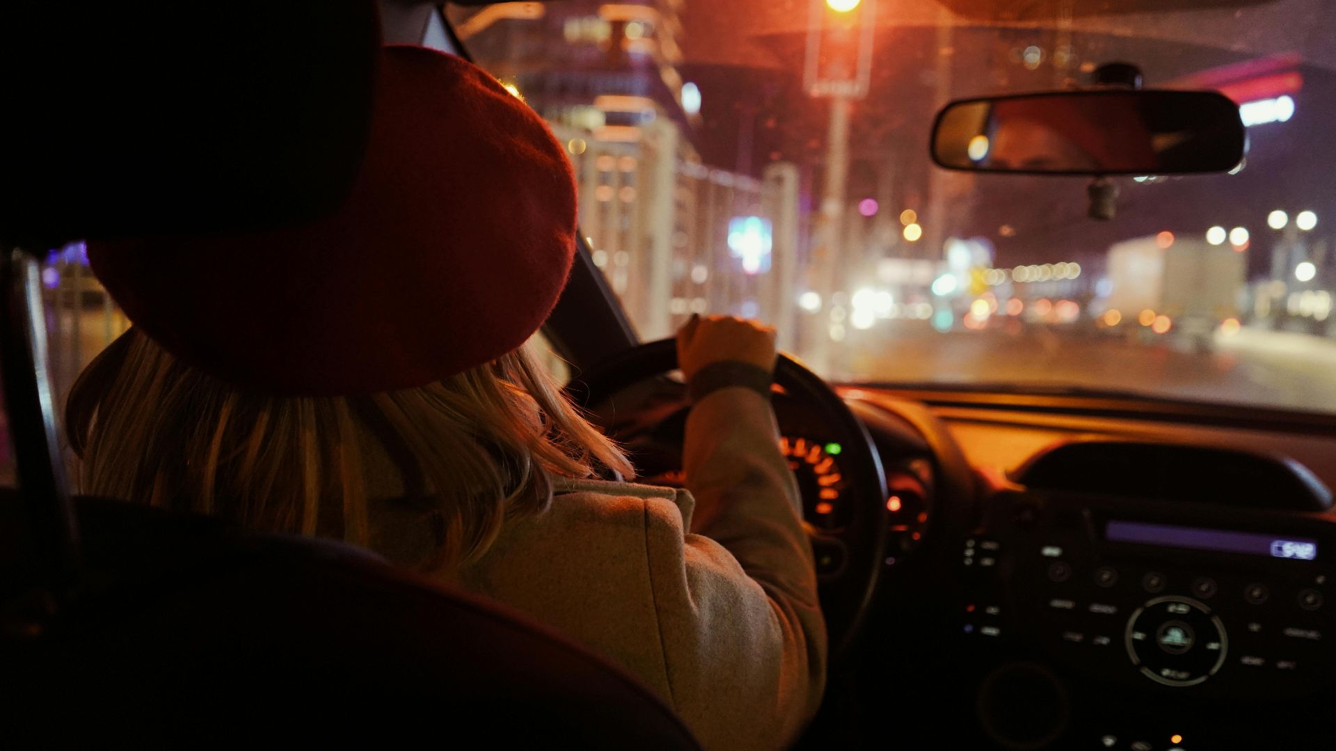 Rear view of a woman driving through Istanbul at night, city lights illuminating the journey.
