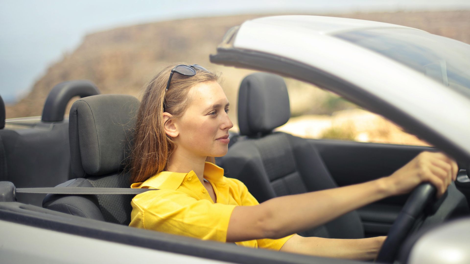A young woman enjoys driving a convertible on a sunny day in Malta.
