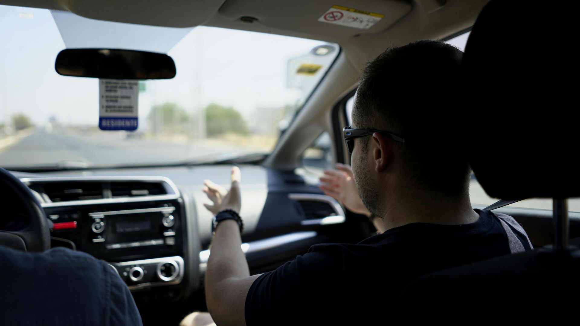 Passenger gesturing while conversing during a car journey on a sunny day.