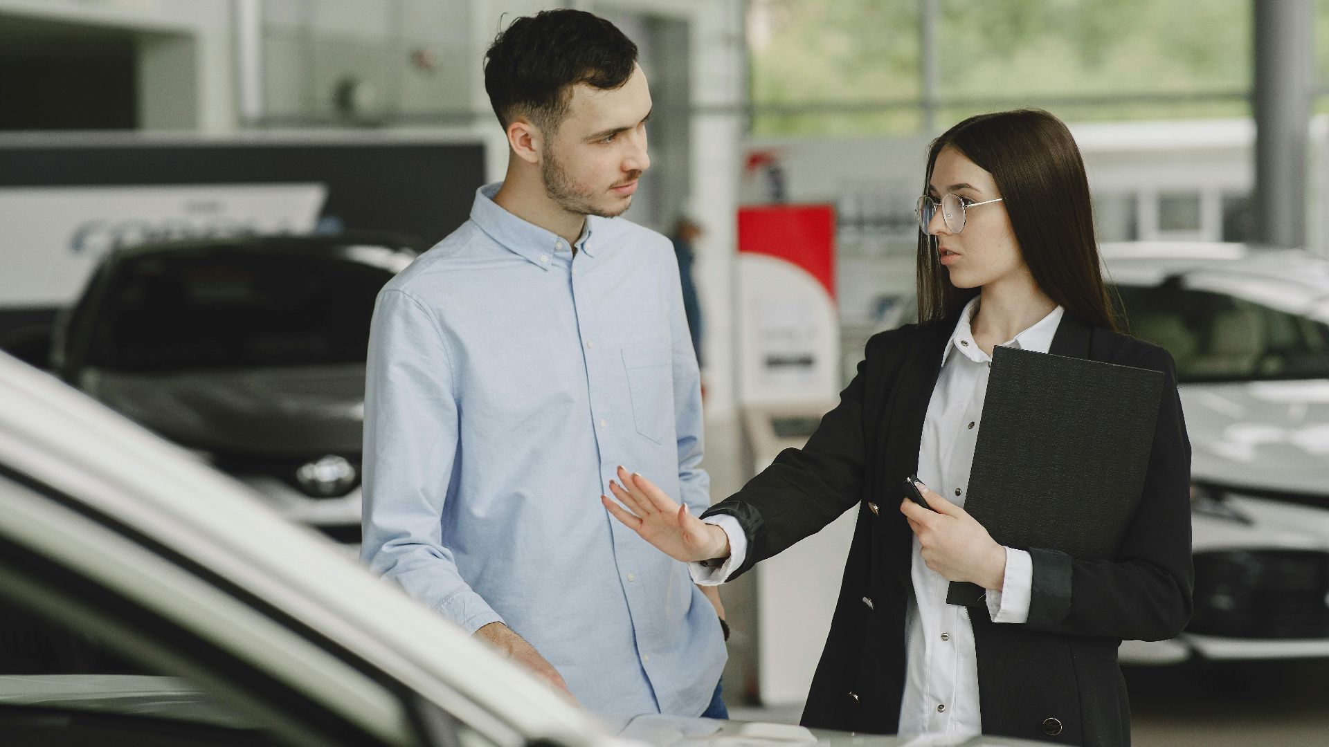 A salesperson and customer discussing car features in a dealership setting.