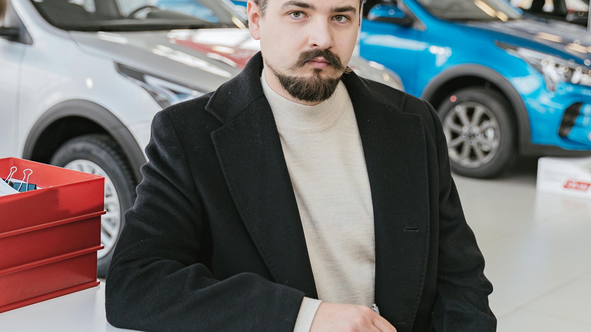 A man in a coat discusses with a sales representative in a bright, modern car showroom.