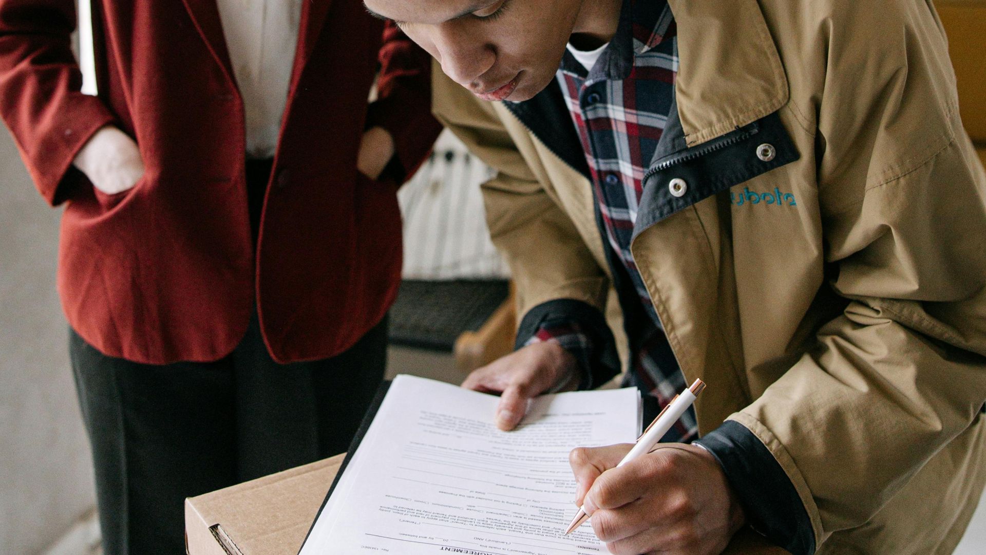 A young man signs a document while a woman observes, set in a modern office environment.