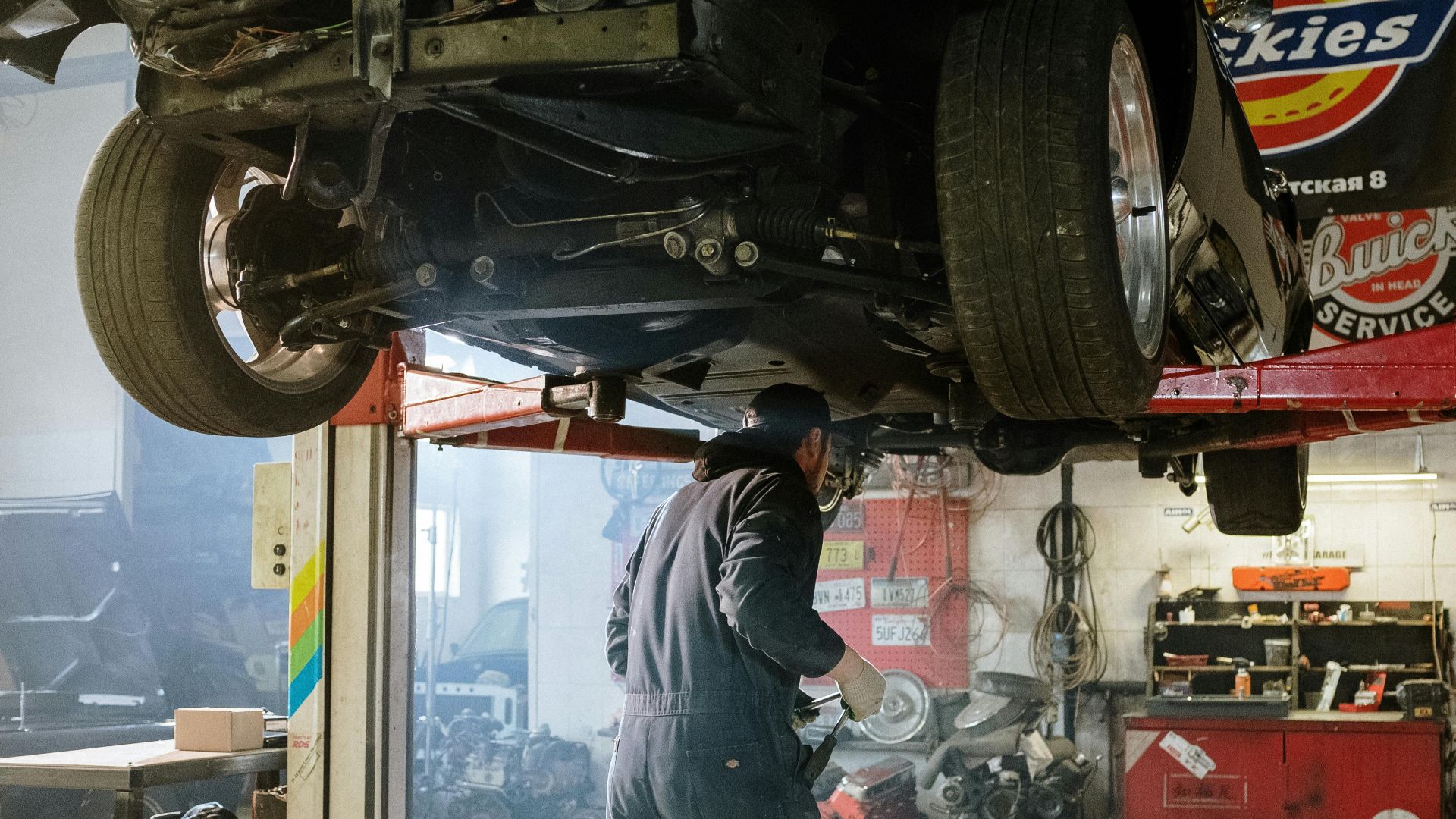 Mechanic repairing a vehicle in a busy workshop with various automotive tools.