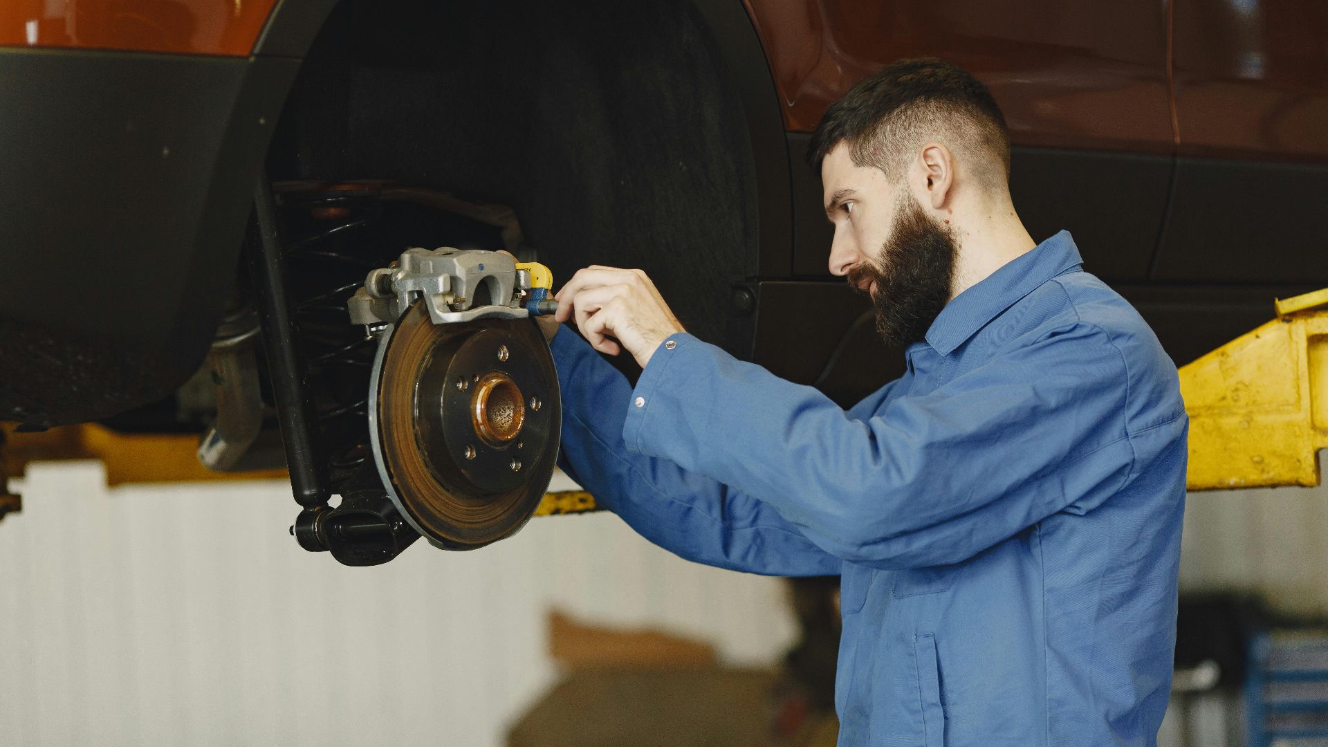 Mechanic in blue uniform performing brake repair on car in modern garage.
