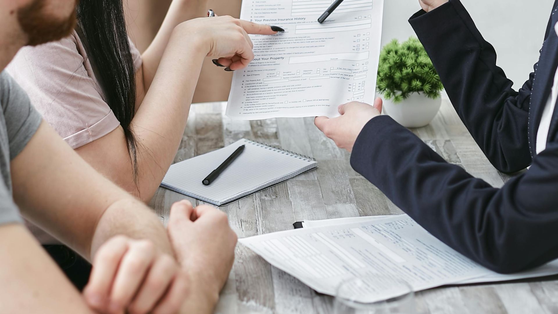 Three adults discuss a home insurance policy at a meeting table indoors.