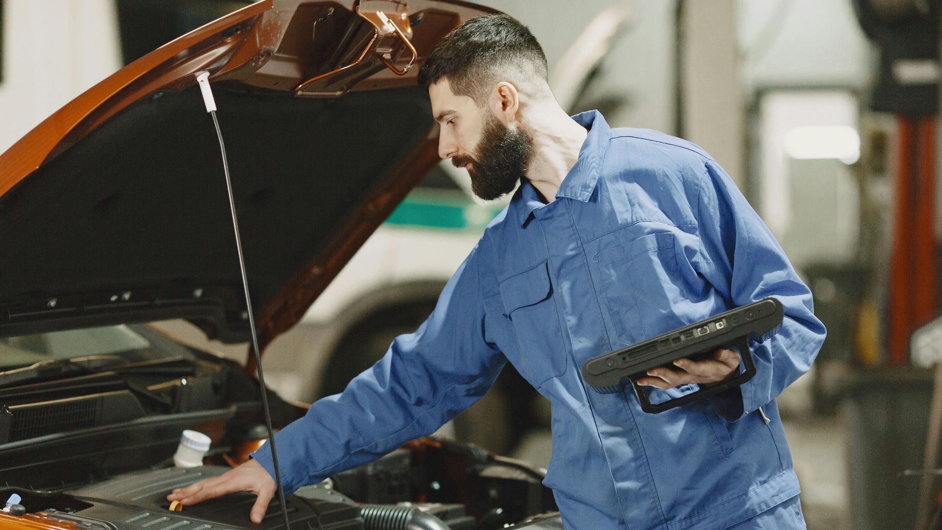 Professional mechanic examining a car engine under an open hood in a garage setting.