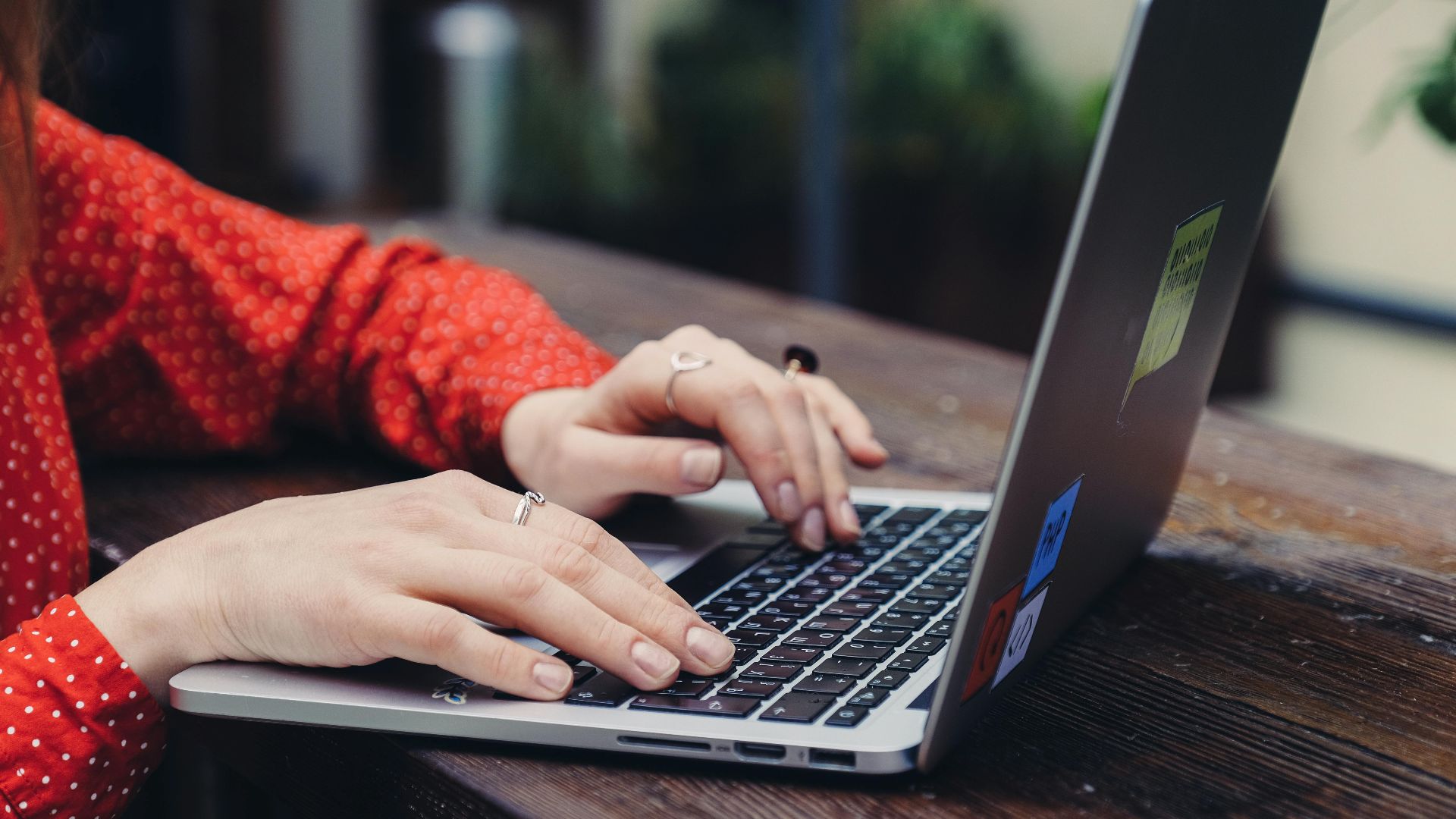 Close-up of hands typing on a laptop placed on a wooden table outdoors.