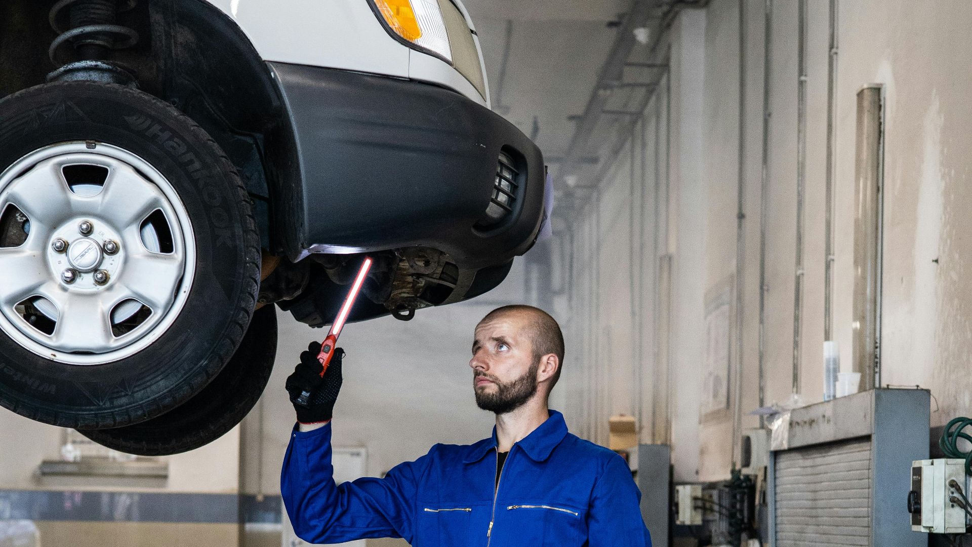 Mechanic in blue coverall inspecting car in auto repair shop. Professional vehicle maintenance in progress.