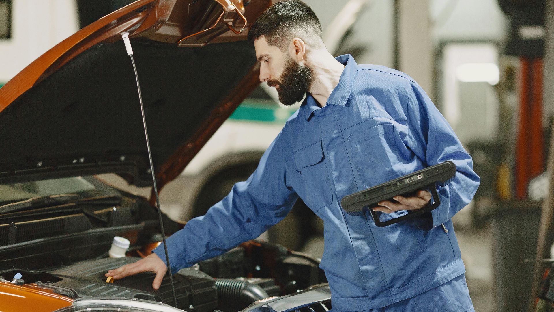 Professional mechanic examining a car engine under an open hood in a garage setting.