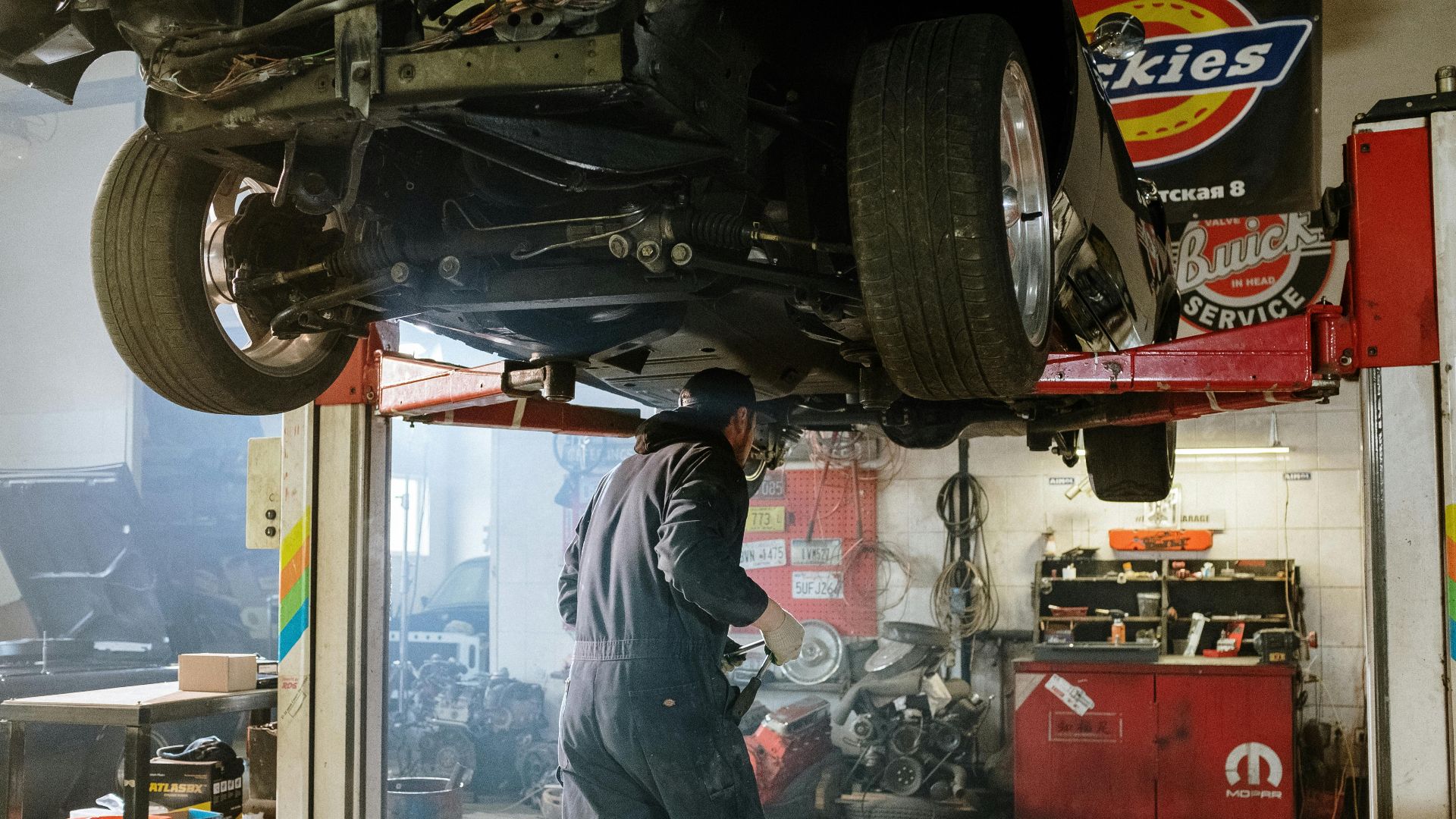 Mechanic repairing a vehicle in a busy workshop with various automotive tools.