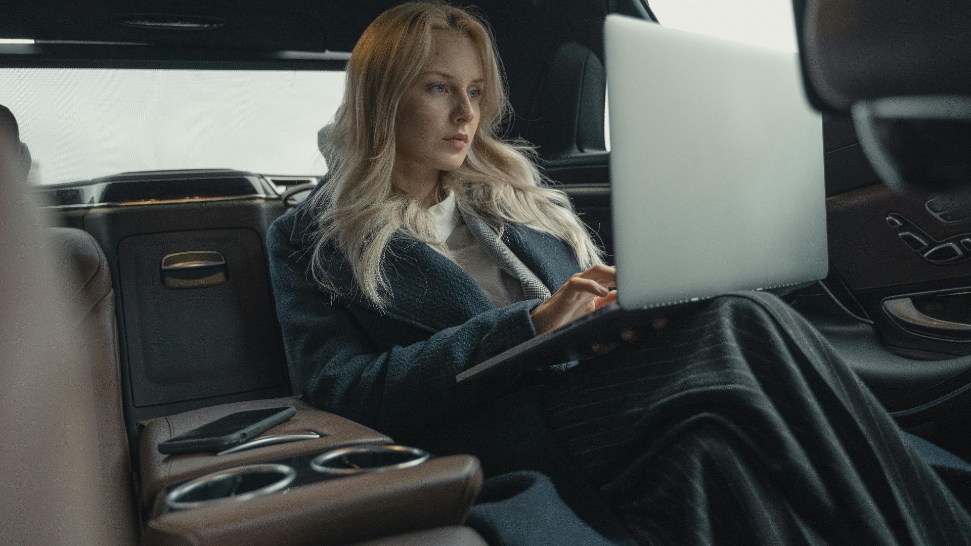 Businesswoman working on her laptop in the back seat of a luxury car.