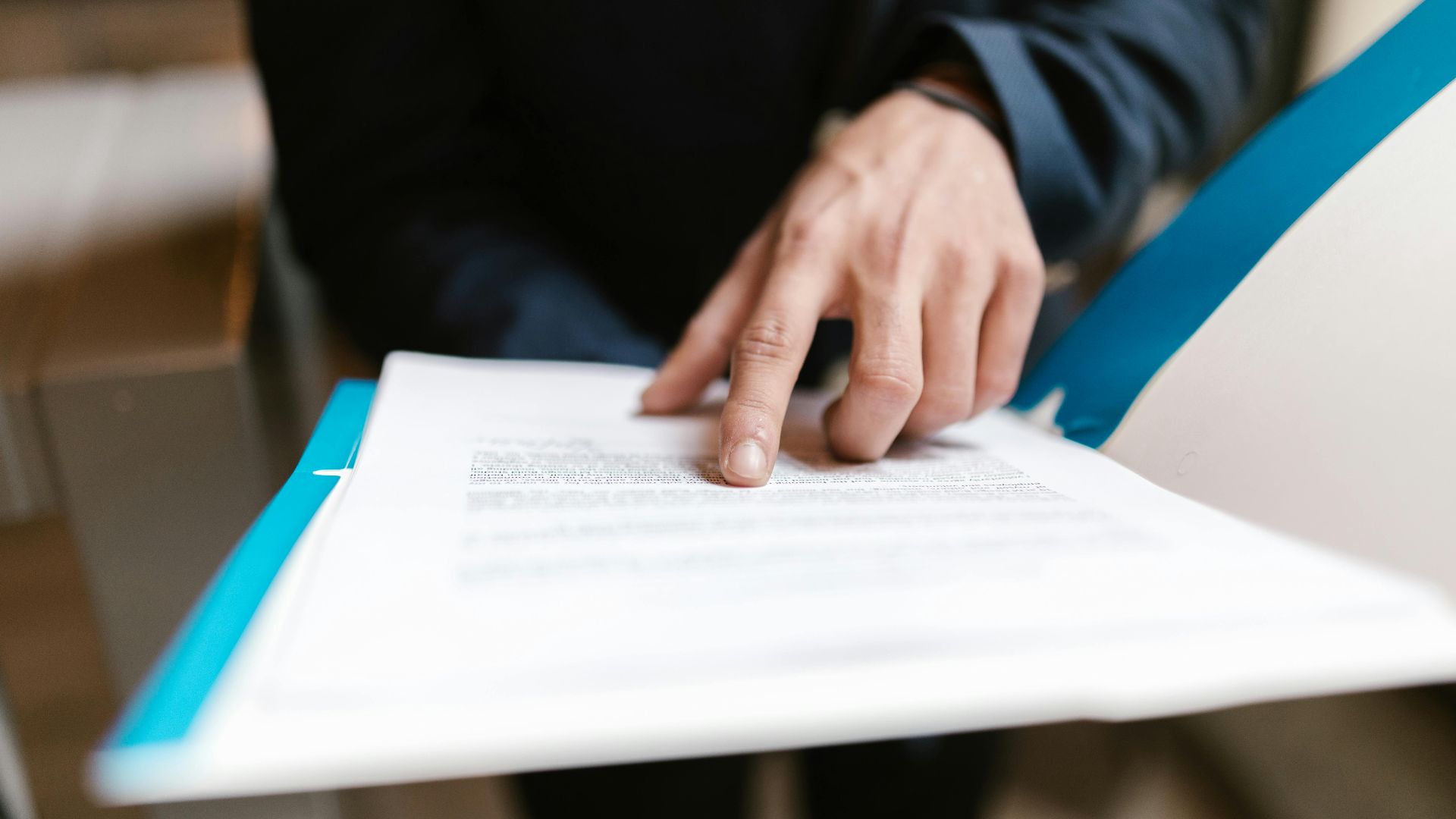 Close-up of a hand pointing at text on a business document in an office environment.