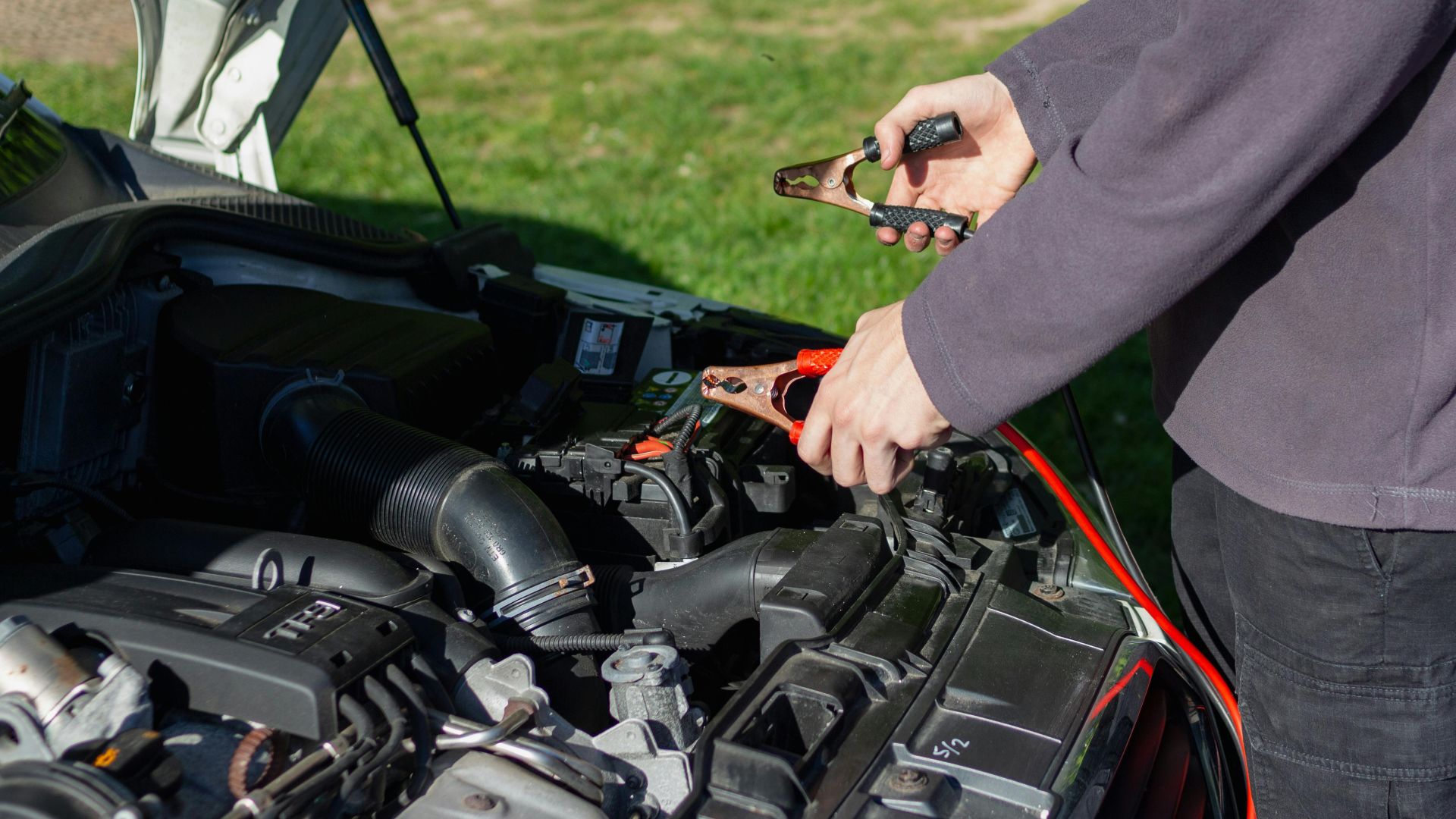 Close-up of mechanic using jumper cables to jump-start a car battery outdoors.