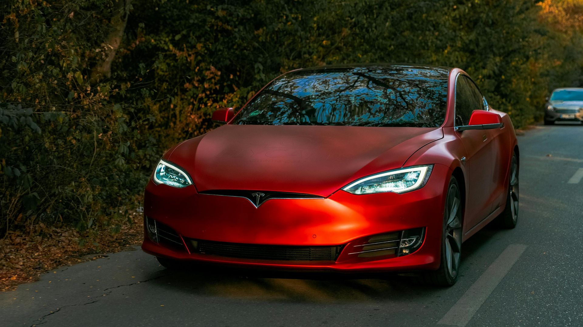 Sleek red electric car driving through a scenic forest road on an autumn day.
