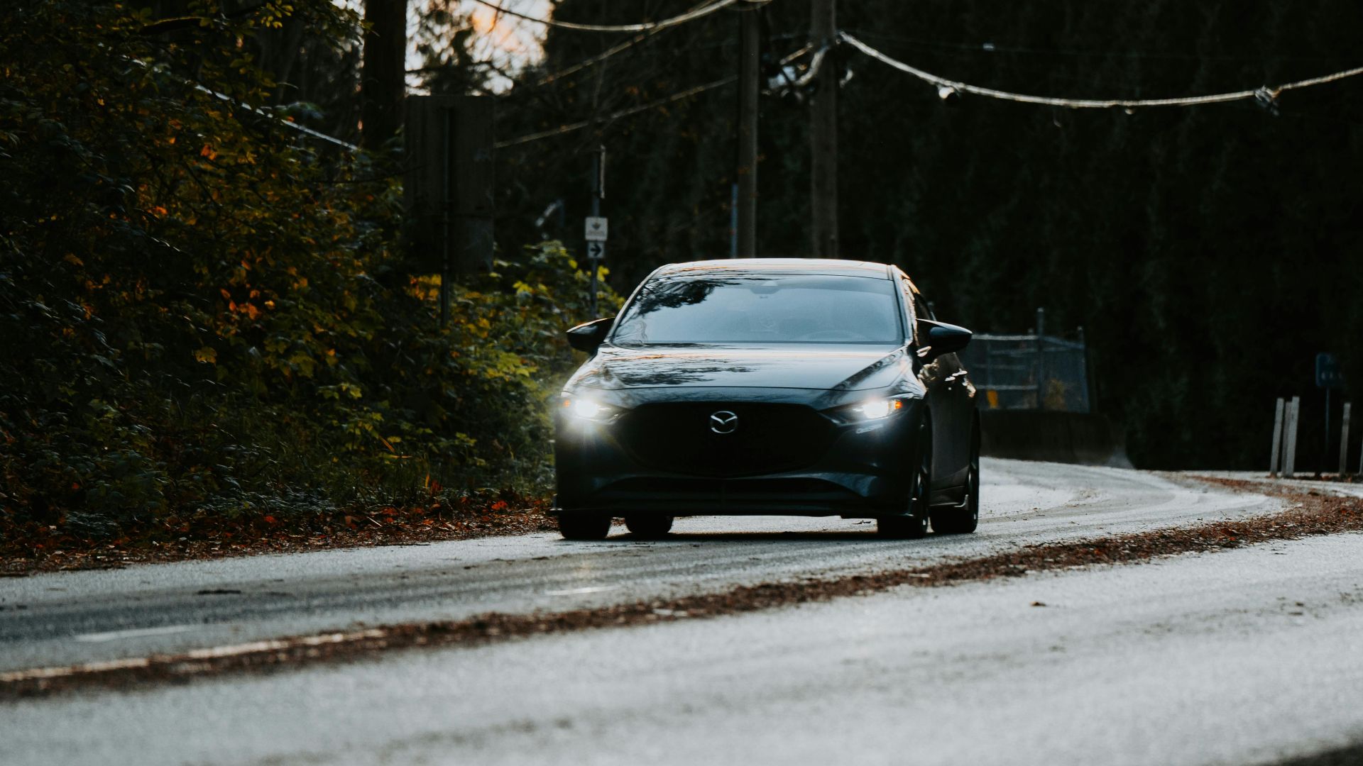 A sleek car with headlights on drives along a scenic forest road at dusk, conveying a sense of adventure.