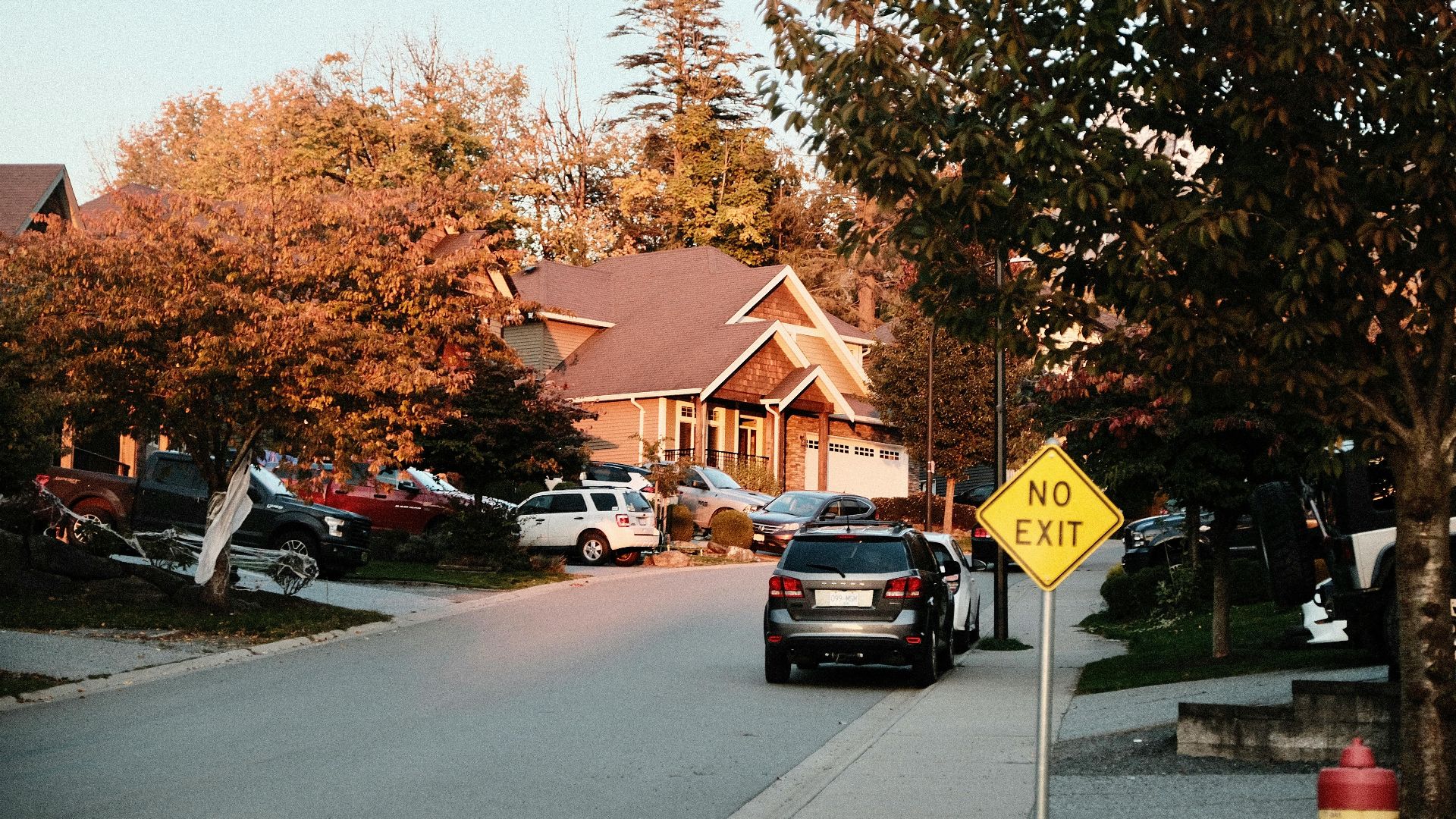 Charming suburban street scene with houses, cars, and a no exit sign in fall.